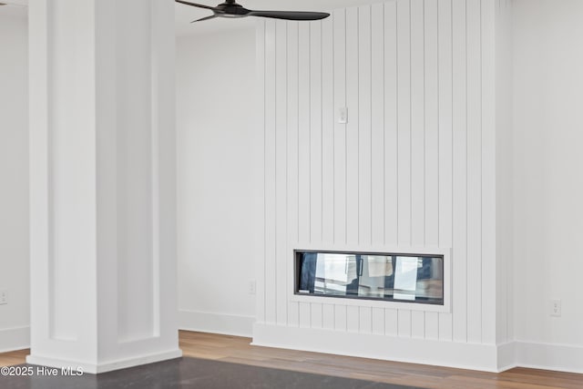 room details with wood finished floors, a glass covered fireplace, a ceiling fan, and baseboards