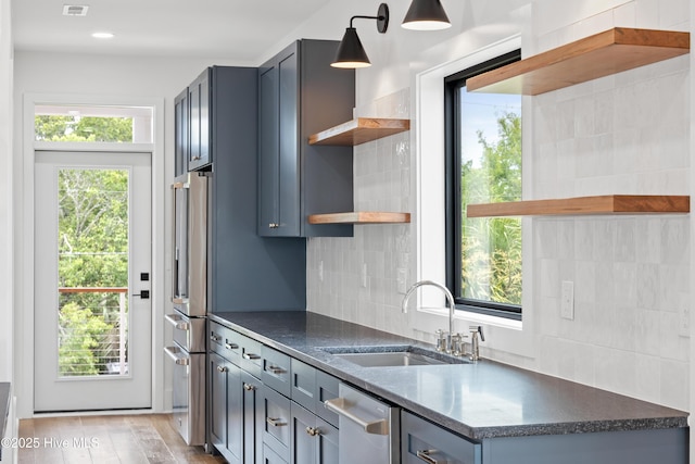 kitchen featuring open shelves, appliances with stainless steel finishes, dark countertops, and a sink