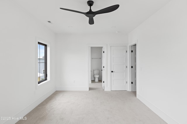 unfurnished bedroom featuring baseboards, ensuite bathroom, a ceiling fan, and light colored carpet