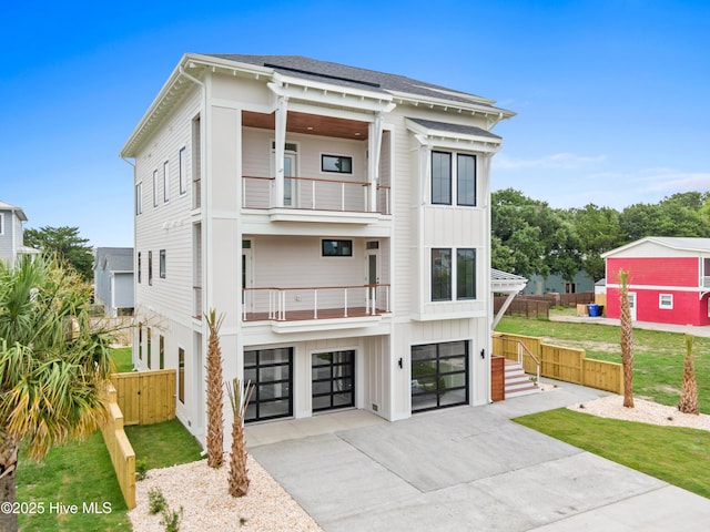 view of front of house featuring driveway, a balcony, an attached garage, fence, and board and batten siding