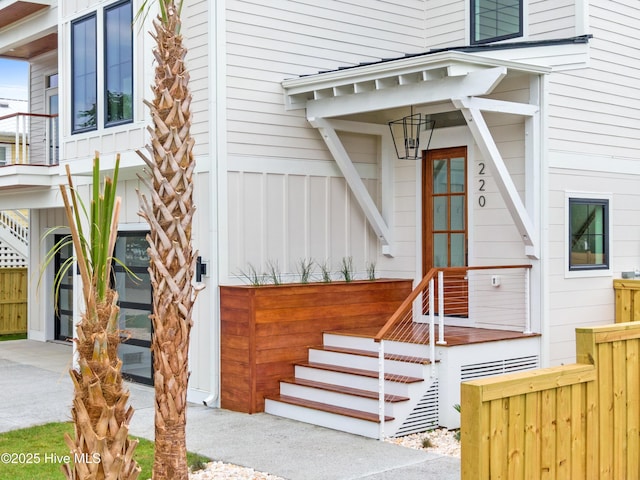 doorway to property with a garage, board and batten siding, and fence