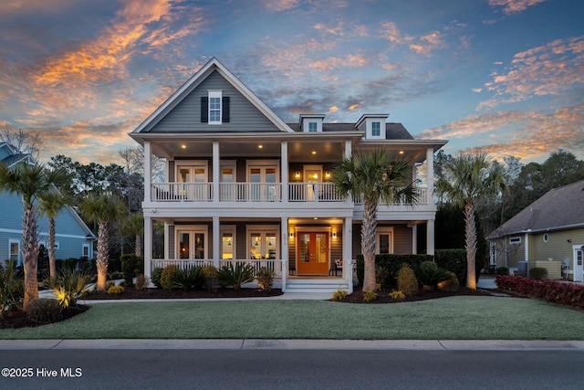 view of front facade featuring french doors, a balcony, covered porch, and a front lawn