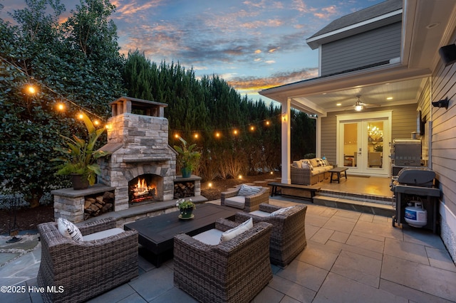 patio terrace at dusk with an outdoor living space with a fireplace, french doors, and area for grilling