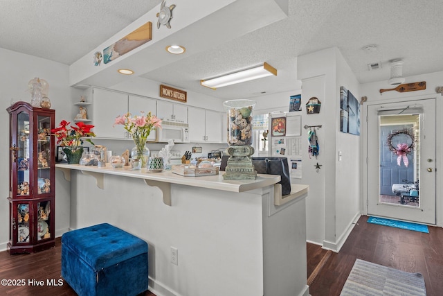 kitchen featuring white microwave, dark wood-type flooring, a peninsula, a textured ceiling, and open shelves