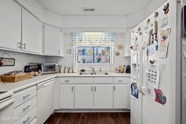 kitchen featuring a textured ceiling, white appliances, dark wood-type flooring, a sink, and visible vents