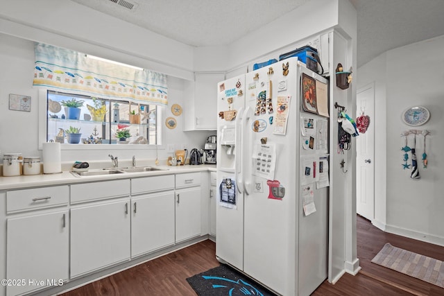 kitchen featuring white fridge with ice dispenser, light countertops, a sink, and dark wood finished floors