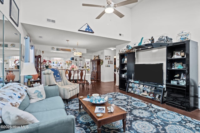 living room with a towering ceiling, wood finished floors, visible vents, and a ceiling fan