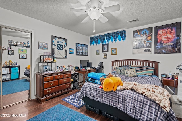 bedroom with a ceiling fan, visible vents, a textured ceiling, and wood finished floors