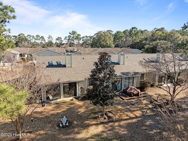 back of house with roof with shingles and a chimney