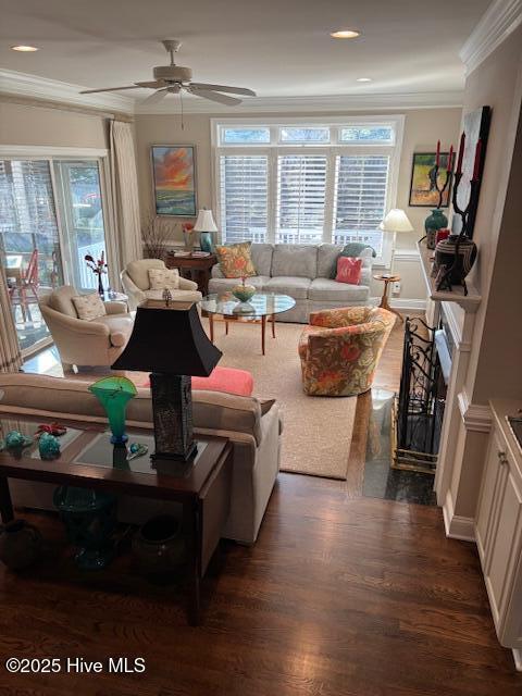 living area with dark wood finished floors, a ceiling fan, crown molding, a fireplace, and recessed lighting