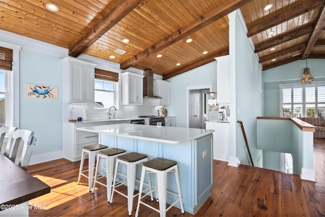 kitchen featuring a center island, light countertops, backsplash, white cabinetry, and wall chimney range hood