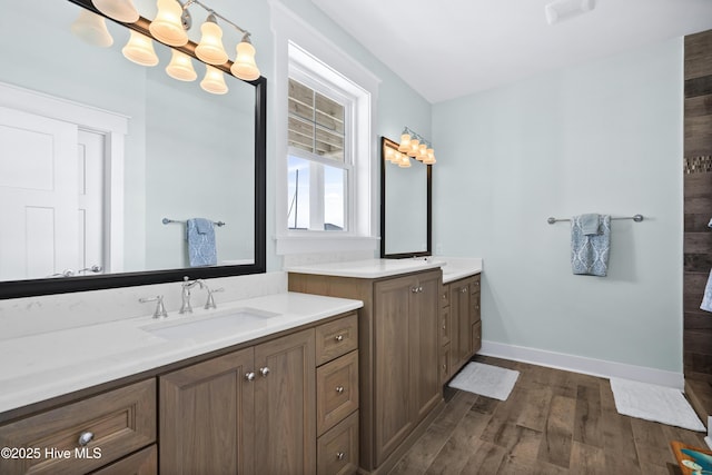 full bath with two vanities, a sink, baseboards, and wood finished floors