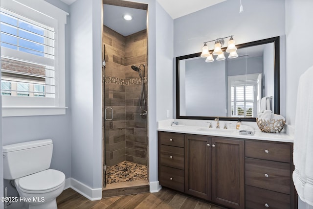 bathroom featuring toilet, wood finished floors, vanity, baseboards, and a stall shower