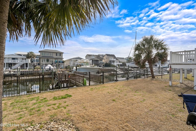 view of dock featuring a lawn, a water view, fence, and a residential view