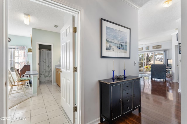 corridor featuring light wood-type flooring, baseboards, and a textured ceiling