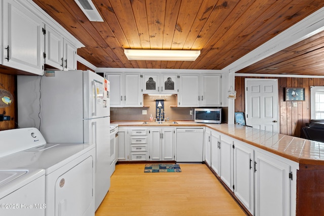 kitchen with stainless steel microwave, white cabinets, white dishwasher, separate washer and dryer, and a peninsula