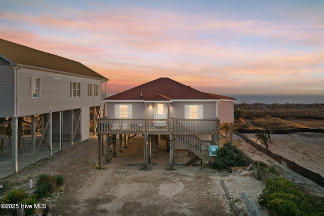 back of house with driveway, roof with shingles, a water view, stairs, and a carport