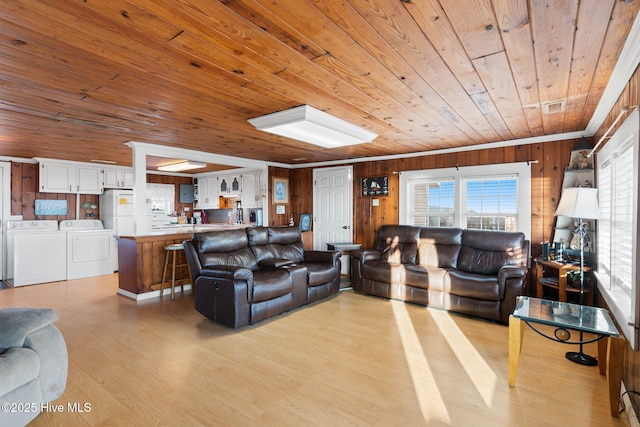 living area featuring wooden ceiling, light wood-style flooring, wood walls, washing machine and clothes dryer, and crown molding