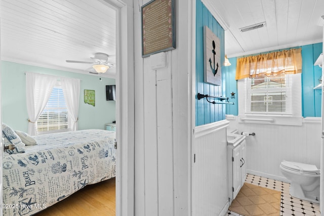 interior space featuring a wainscoted wall, visible vents, ornamental molding, and ceiling fan