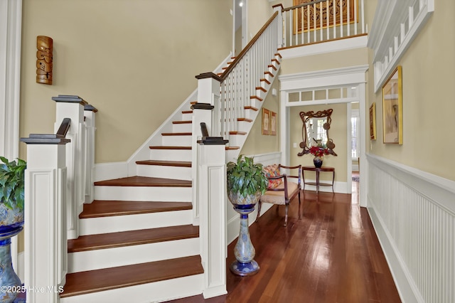 stairs featuring wood finished floors, a high ceiling, and wainscoting