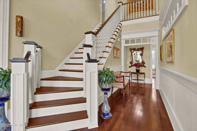 stairway featuring a wainscoted wall, wood finished floors, and a towering ceiling