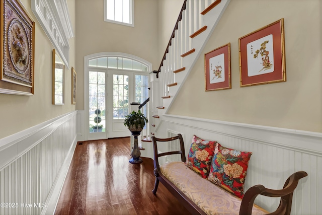 entryway with a wainscoted wall, wood finished floors, a decorative wall, stairway, and a towering ceiling