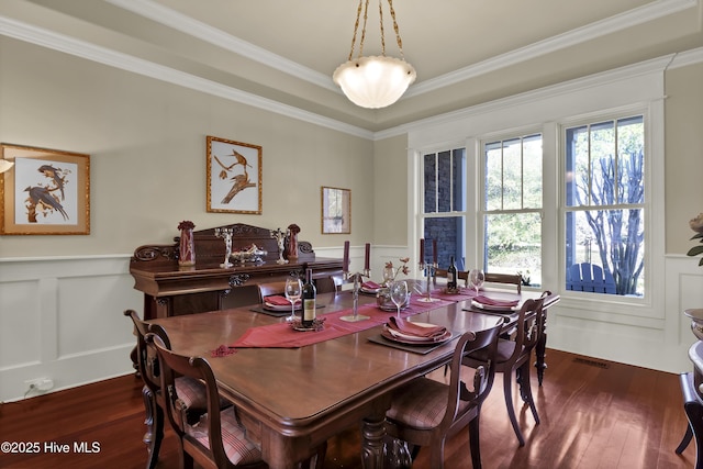 dining room featuring dark wood-style floors, a decorative wall, wainscoting, and ornamental molding