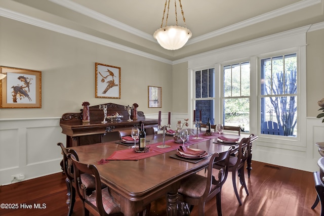 dining room featuring ornamental molding, dark wood-style flooring, a wainscoted wall, and a decorative wall