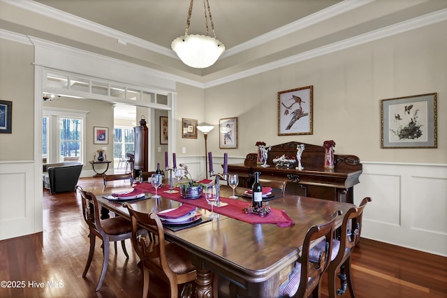 dining room featuring ornamental molding, a decorative wall, wood finished floors, and wainscoting