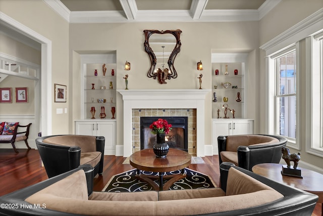 living area featuring crown molding, wood finished floors, a tiled fireplace, built in features, and beam ceiling