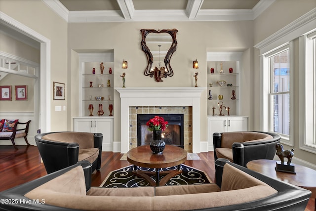 living room featuring a tile fireplace, built in features, ornamental molding, beam ceiling, and dark wood finished floors