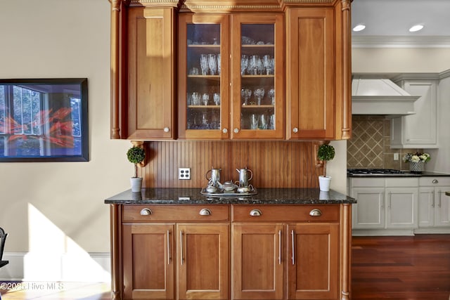 bar with black gas cooktop, ornamental molding, decorative backsplash, dark wood-style floors, and wall chimney exhaust hood