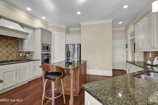 kitchen with appliances with stainless steel finishes, dark wood-style flooring, premium range hood, dark stone countertops, and recessed lighting