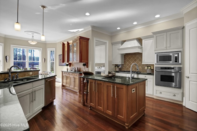 kitchen with glass insert cabinets, appliances with stainless steel finishes, dark stone countertops, hanging light fixtures, and premium range hood