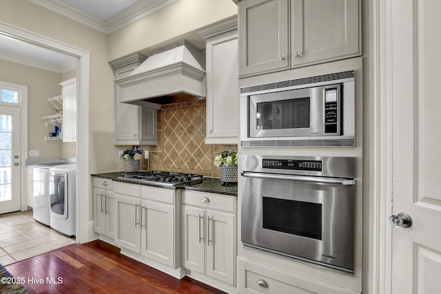 kitchen featuring tasteful backsplash, washer and clothes dryer, custom exhaust hood, stainless steel appliances, and crown molding