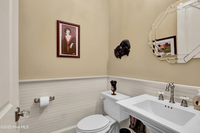 half bathroom with wainscoting, a sink, and toilet