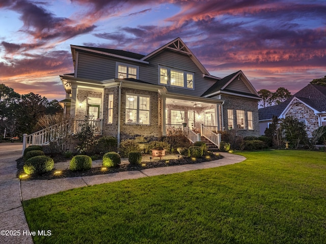craftsman house featuring covered porch, a yard, brick siding, and stairway