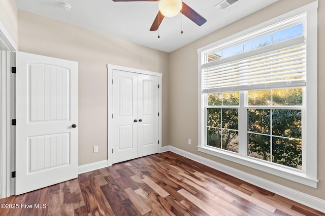 unfurnished bedroom with a ceiling fan, visible vents, baseboards, a closet, and dark wood-style floors