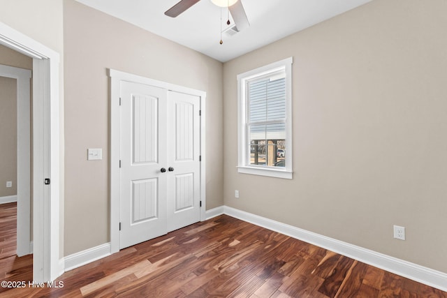 unfurnished bedroom with ceiling fan, a closet, dark wood finished floors, and baseboards