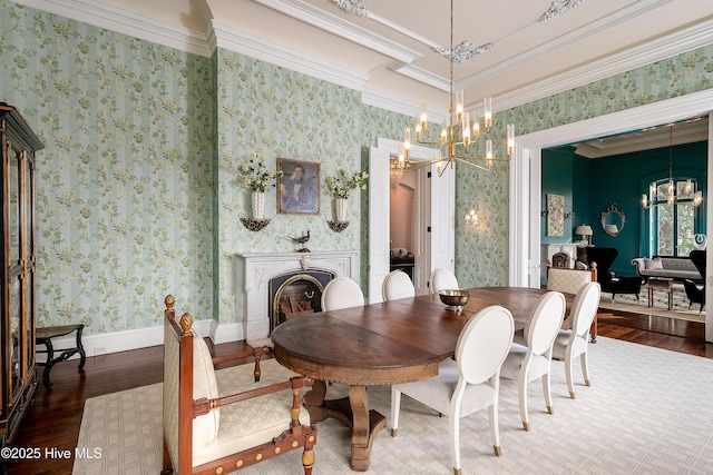 dining space with wallpapered walls, ornamental molding, wood finished floors, a fireplace, and a chandelier