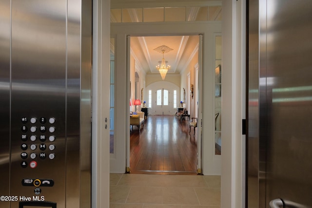 hall with elevator, tile patterned flooring, ornamental molding, and an inviting chandelier