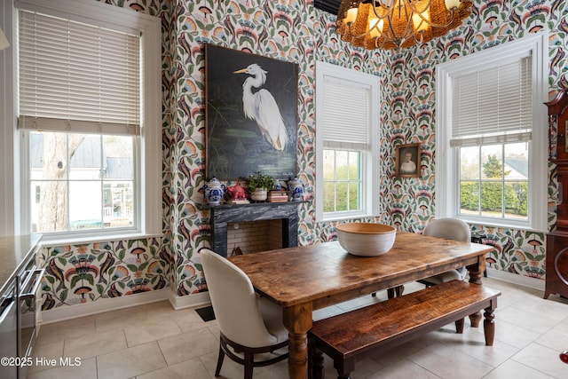 dining room featuring wallpapered walls, light tile patterned floors, baseboards, a fireplace, and a chandelier