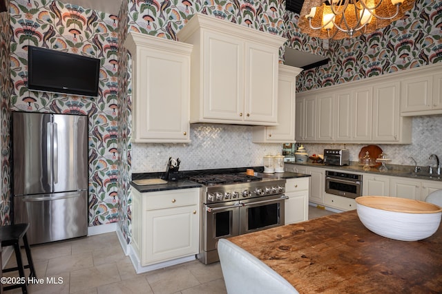 kitchen featuring stainless steel appliances, backsplash, a sink, and wallpapered walls