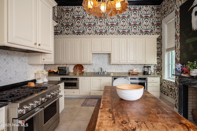 kitchen featuring light tile patterned flooring, a sink, white cabinets, appliances with stainless steel finishes, and wallpapered walls