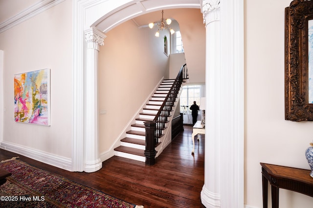 stairway with arched walkways, decorative columns, baseboards, and wood finished floors