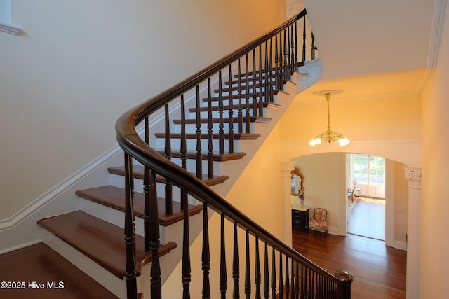 stairs with baseboards, arched walkways, wood finished floors, a high ceiling, and a chandelier