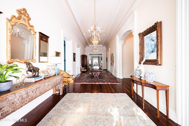 hallway with dark wood-style floors, arched walkways, crown molding, a notable chandelier, and baseboards