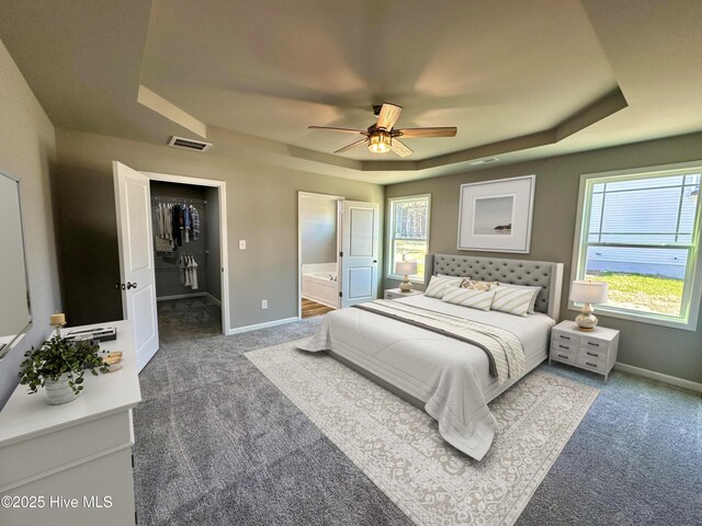 unfurnished bedroom featuring visible vents, ensuite bath, dark carpet, baseboards, and a raised ceiling