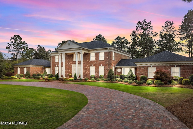 neoclassical / greek revival house featuring a lawn, decorative driveway, and brick siding