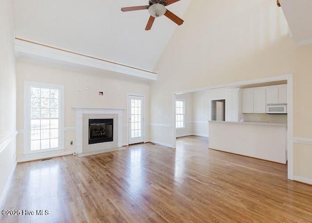 unfurnished living room with ceiling fan, high vaulted ceiling, a fireplace with flush hearth, visible vents, and light wood finished floors